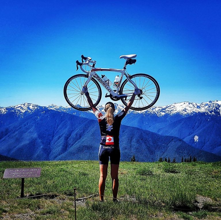 Kara Hobby holding bike above her head at the top of Hurricane Ridge on Canada Day