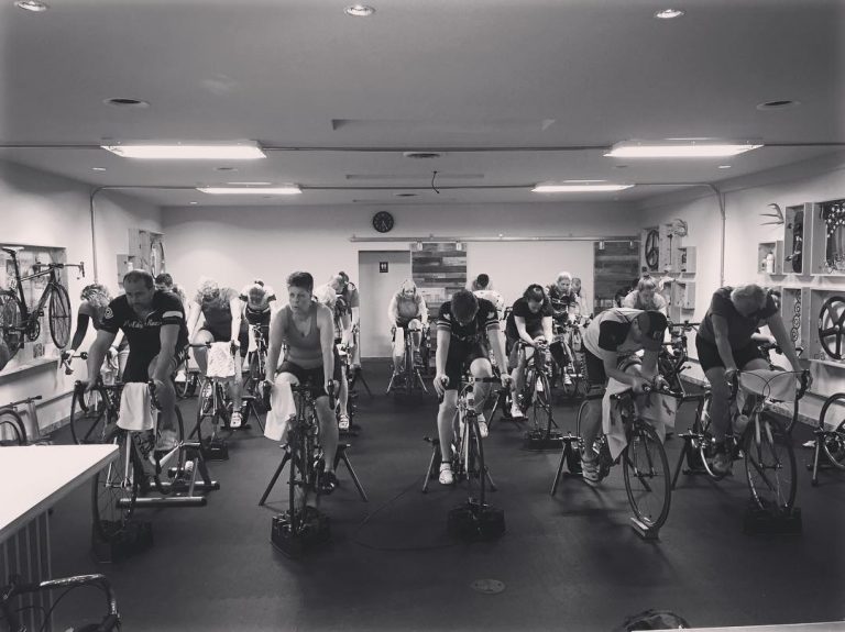 Black and white photo of a room full of people on stationary bikes.