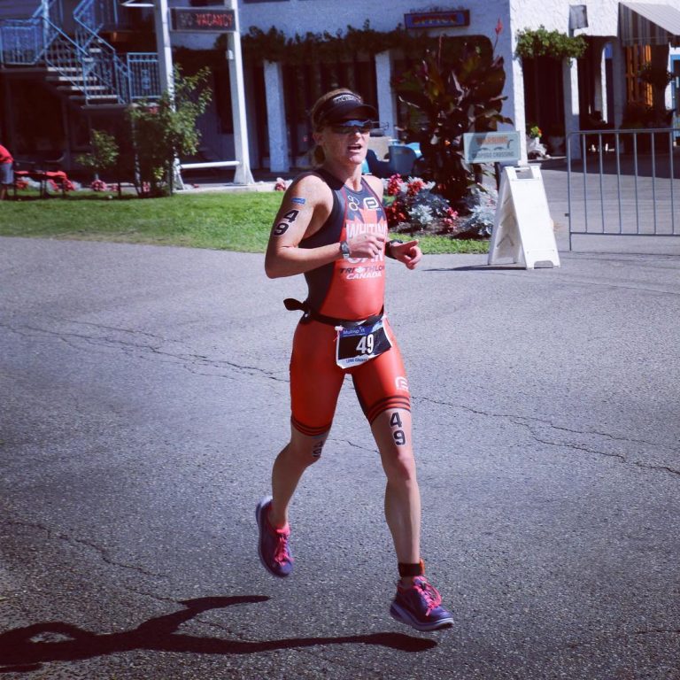 A woman in orange running gear (tank and shorts) running along a road on a sunny day.