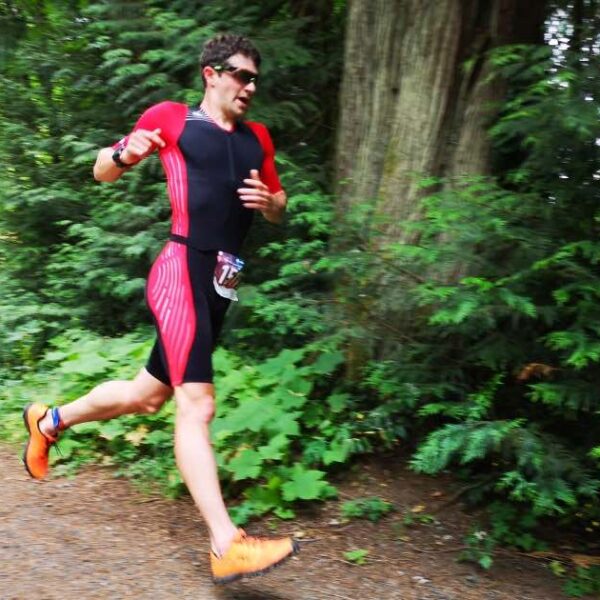 A man in a black and white triathlon body suit running along a forest trail.