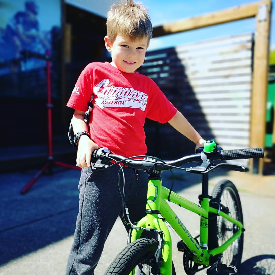 A young boy standing beside his green bike and smiling down at the camera.
