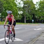 A young woman rides her bike towards the camera along ring road on the UVic campus.
