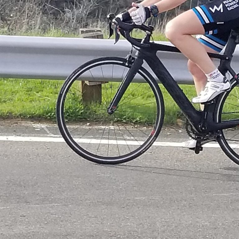 Partial view of a bicycle, front wheel, handlebar and the biker's legs visible, on a road