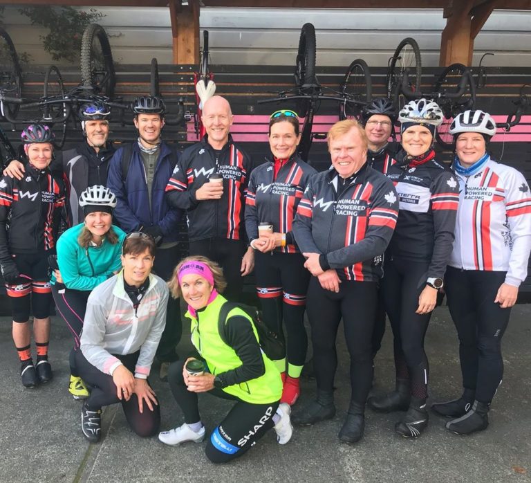 About a dozen people in running and biking gear, some of them with helmets on standing and kneeling as a group posing.