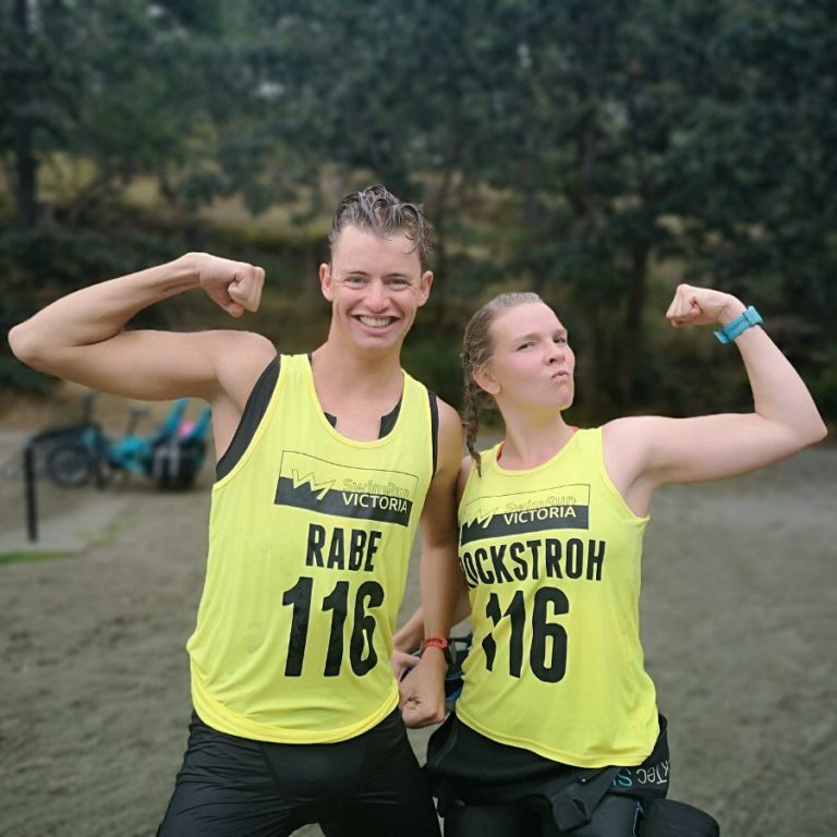 A male and a female athlete, both in yellow running jerseys stand side by side posing with their forearms curled up to show off their biceps.