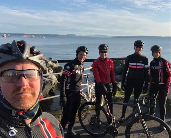 Four bicyclists posing as a selfie with their bikes beside an ocean under blue skies