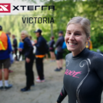 A woman smiling in a wetsuit on a beach.