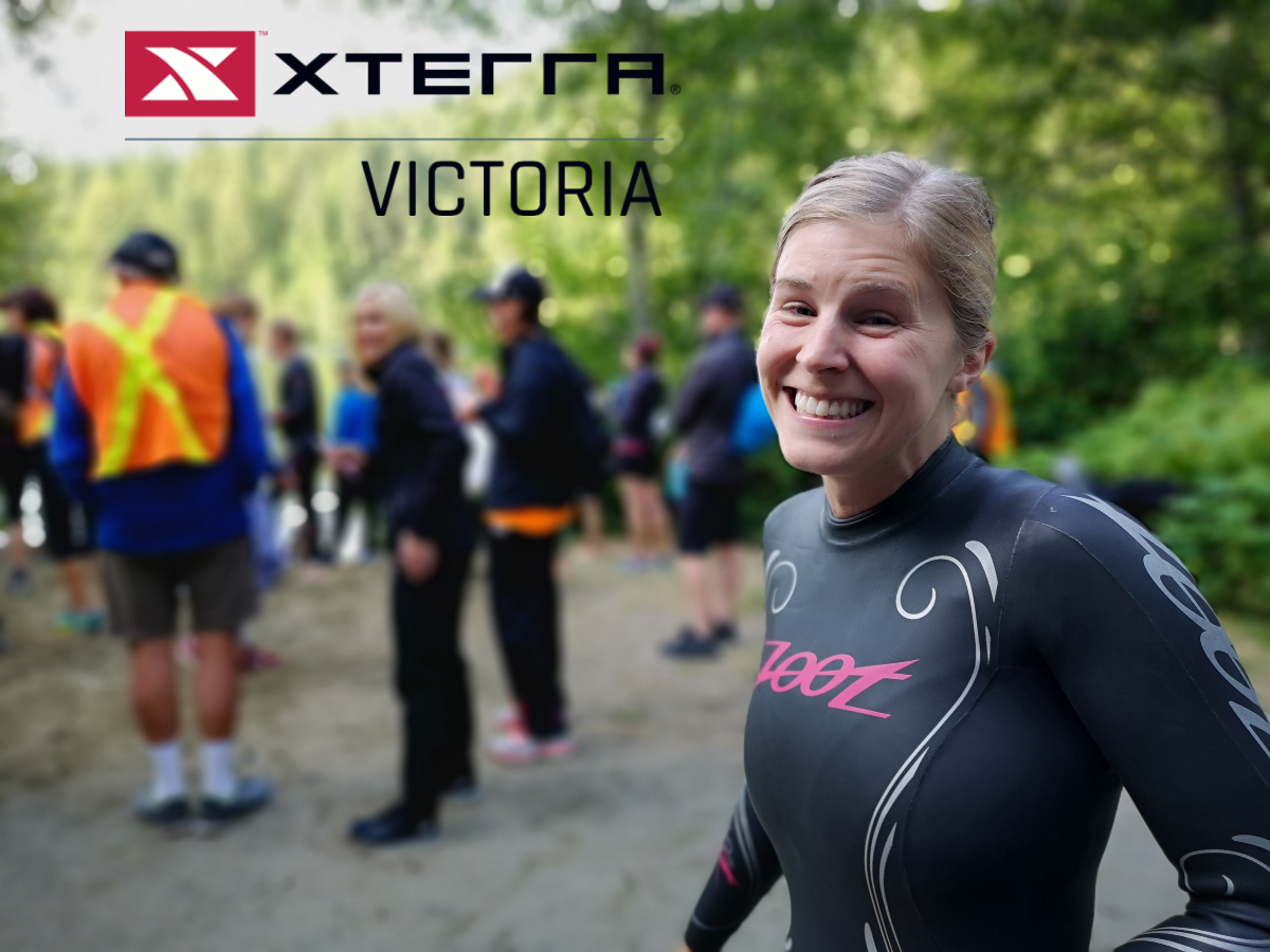 A woman smiling in a wetsuit on a beach.