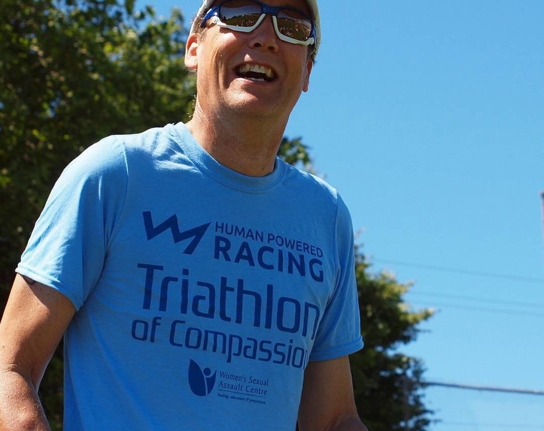 A participant of the Triathlon of Compassion has a big smile while wearing a race t-shirt.