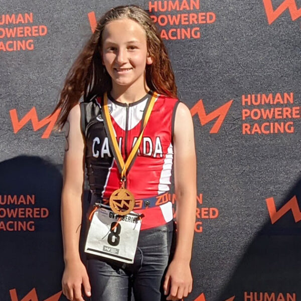 A young athlete stands in front of the podium with her medal.