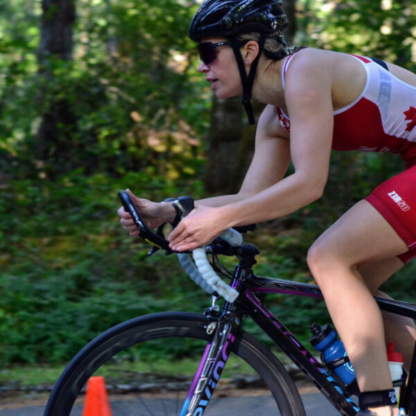 A triathlete on her bicycle sets out on the course at the Cowichan Challenge with the lush green forest in the background.