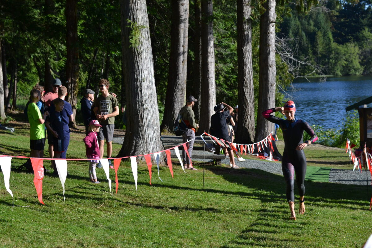Female triathlete running up hill undoing her wetsuit.