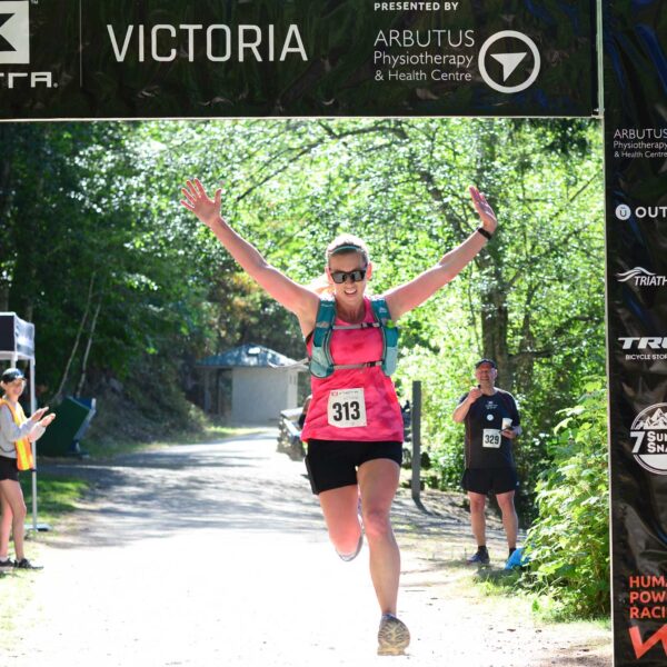 First place women's finisher flies across the finish line, arms in the air.