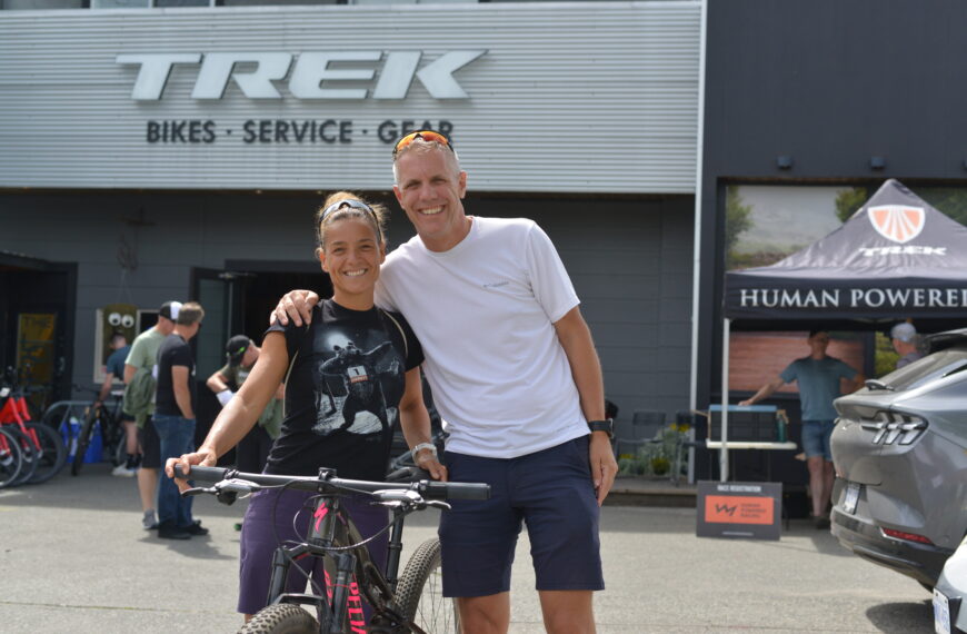 A racer and her partner pose below the TREK sign with her bicycle.