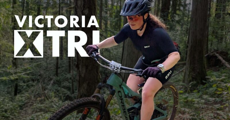 Victoria X Tri logo over top of a cyclist burning down a single track forest course.