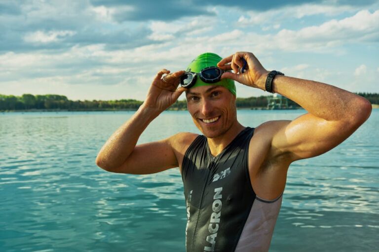 Confident male athlete adjusting goggles at a lake during a sunny day, ready for training.